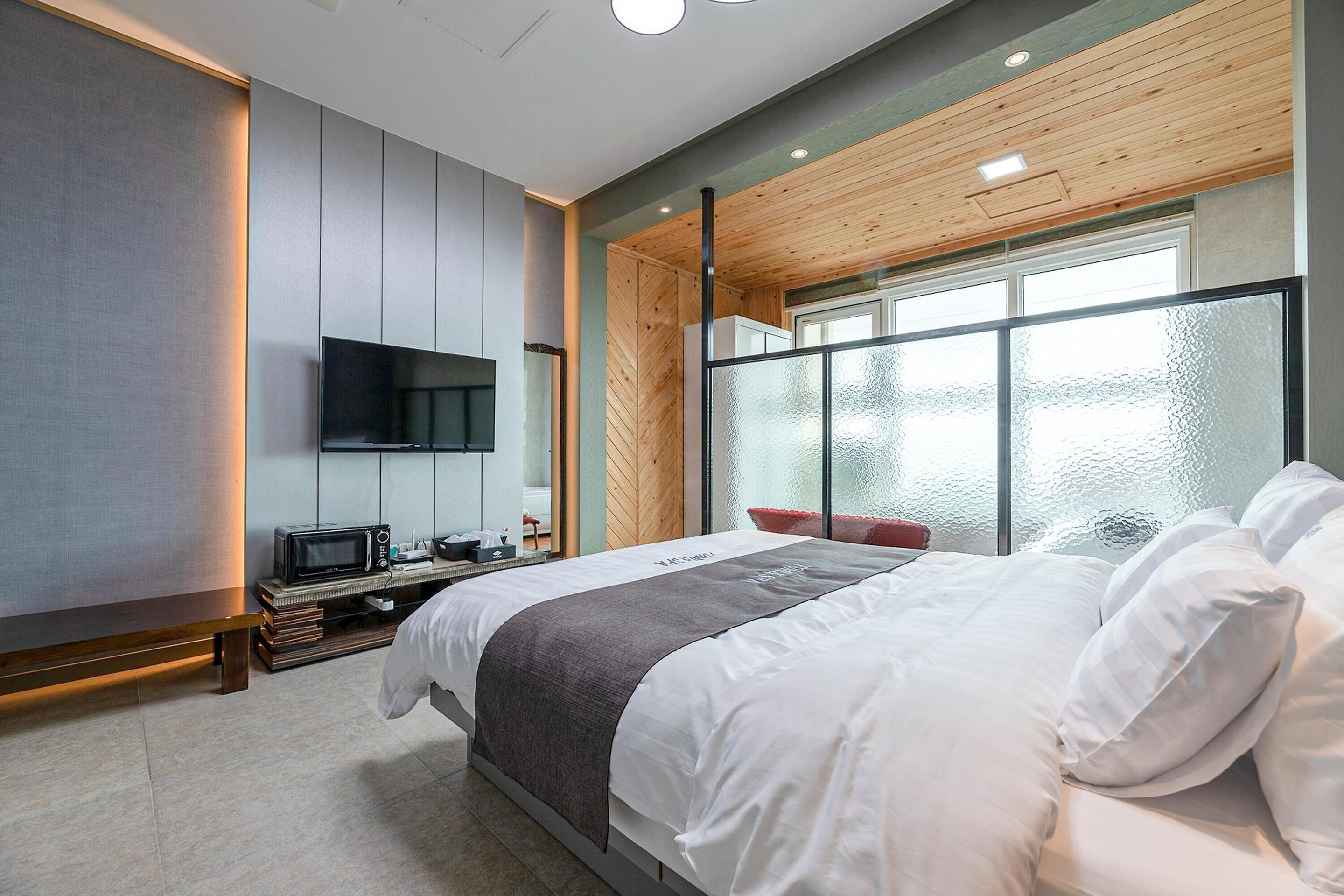 Un dormitorio moderno con una cama grande, un televisor de pantalla plana, un banco y vistas al exterior a través de un ventanal.