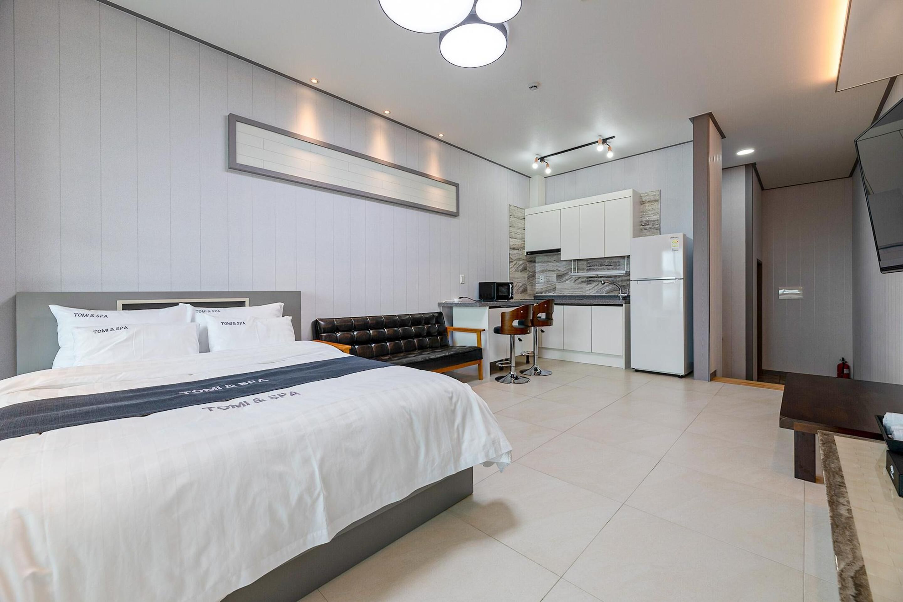 Quarto de hotel moderno com uma cama grande, cozinha compacta, área de estar e televisão.