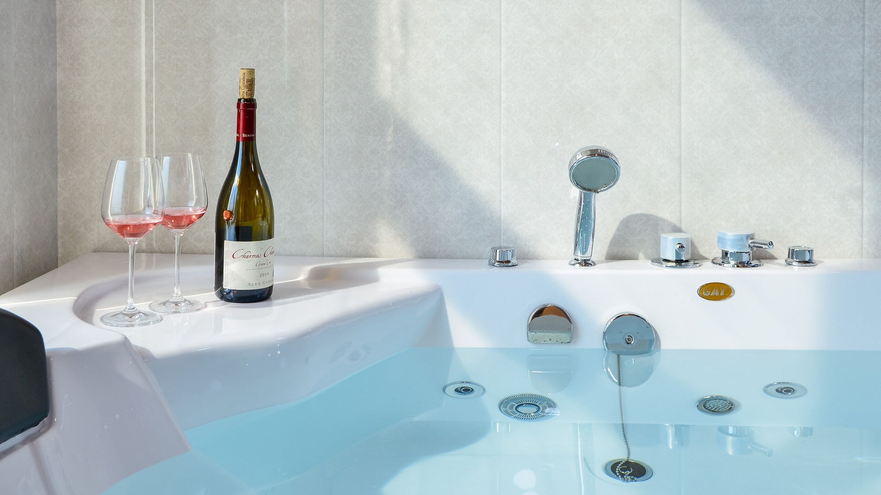 A bathroom with a bathtub, a bottle of wine, and two glasses of red wine.