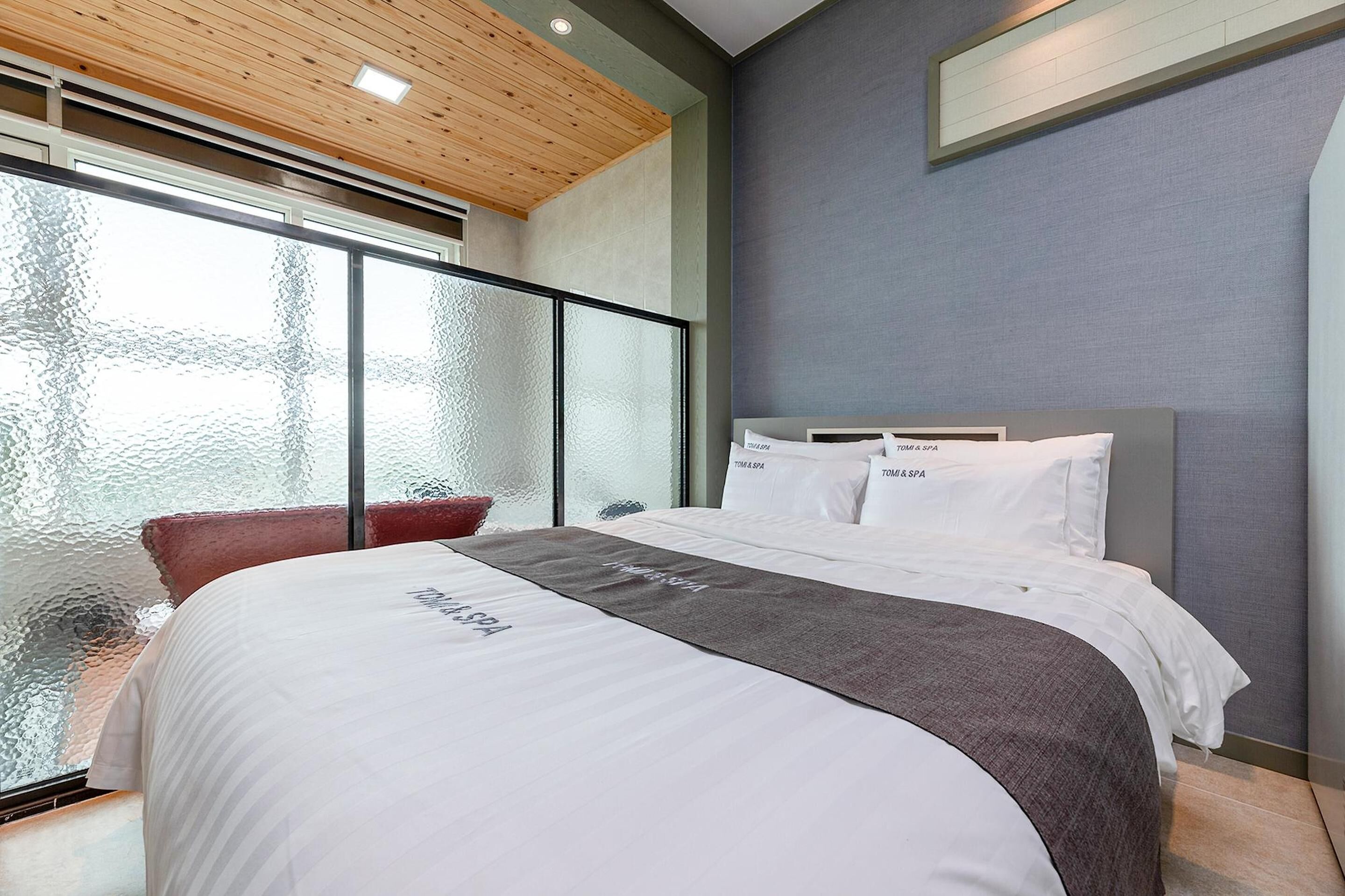 Una habitación de hotel moderna con una cama grande, un separador de vidrio y vistas a la ciudad.