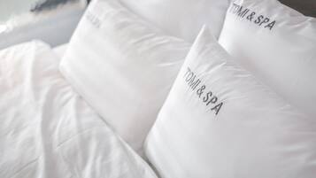 A bed with white bedding and pillows that have "TOMI & SPA" embroidered on them.