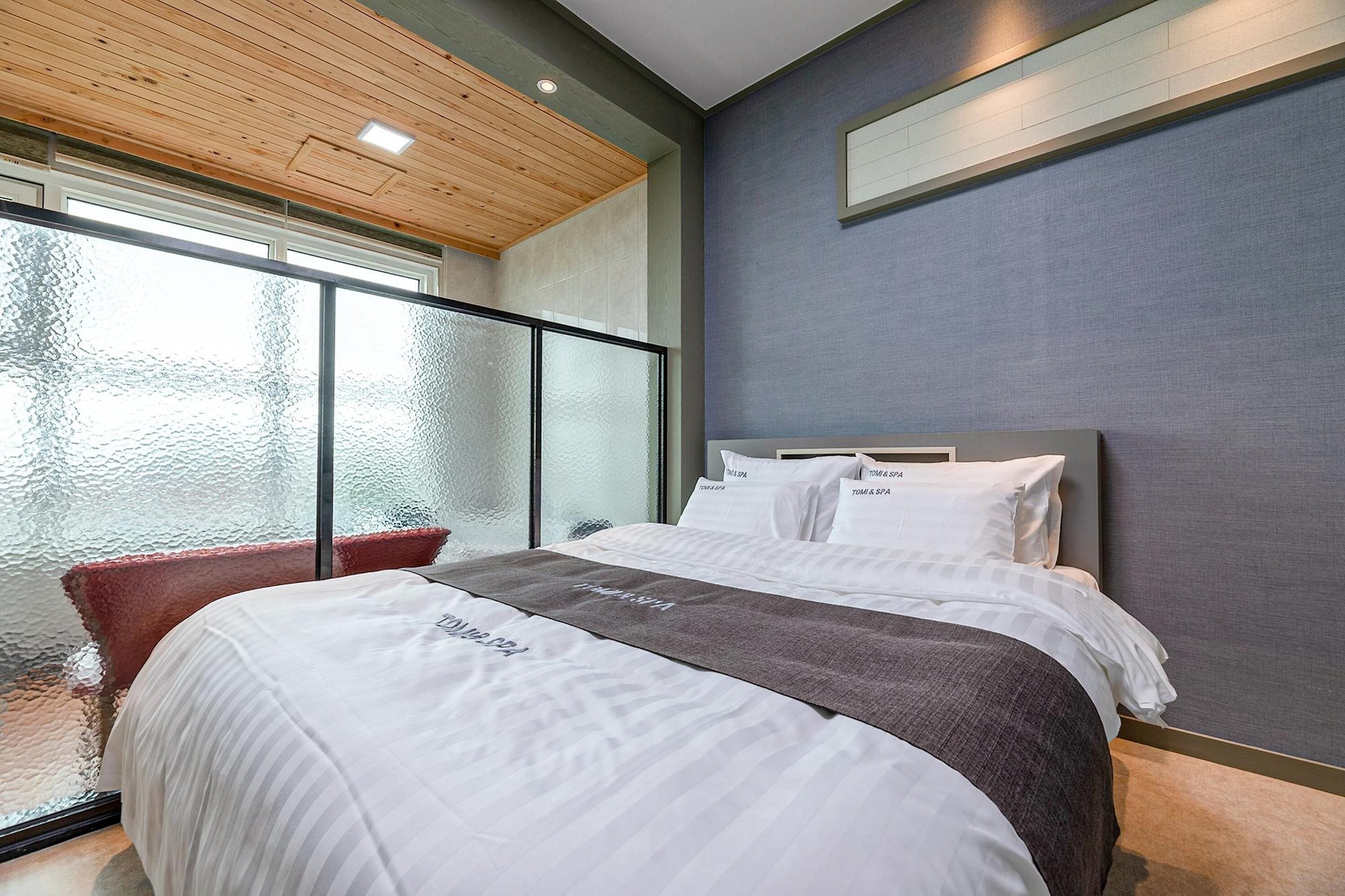 Ein modernes Hotelzimmer mit einem großen Bett, einer Glastür, die auf einen Balkon führt, und einer Wand mit Grau-Struktur.