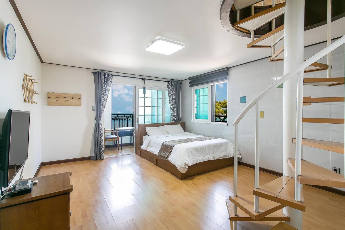 Une chambre à coucher comprenant un lit, une télévision, un bureau, une chaise, un balcon et un escalier.