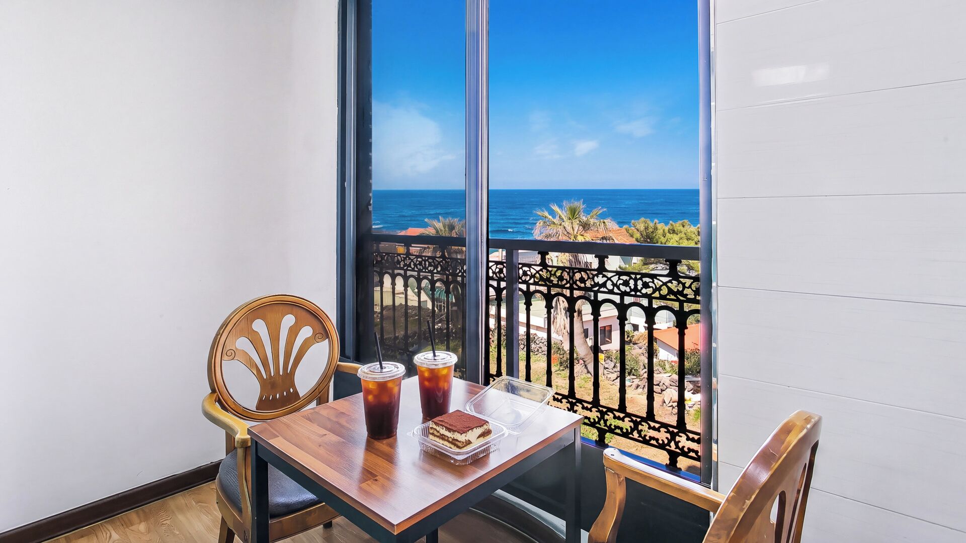 Un balcón con vista al océano, una mesa con bebidas y un postre, y dos sillas.