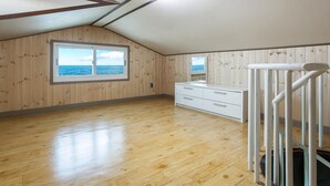 Ein Zimmer mit Holzwänden, einem großen Fenster mit Meerblick, einem weißen Schminktisch und einem Metallgeländer.