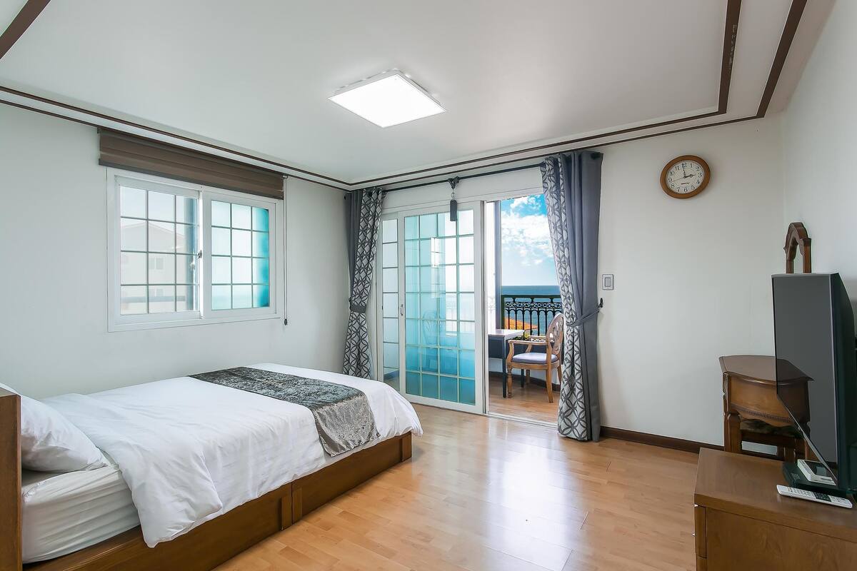 Une chambre à coucher avec un lit, un bureau, une chaise, une horloge et une vue sur l’extérieur.
