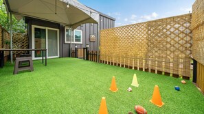 Een achtertuin met kunstgras, een patio tafel en een overdekte zithoek.
