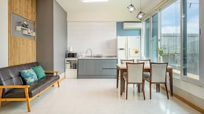 Un espace de vie moderne comprenant un canapé, une table à manger, des chaises, un coin cuisine et une grande fenêtre donnant sur un paysage agréable.