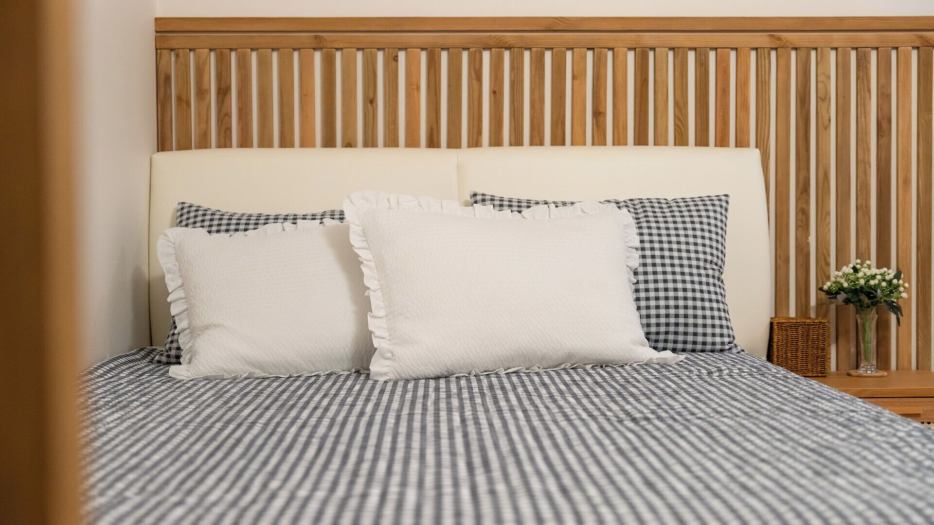 A bed with a striped bedspread, two pillows with ruffled edges, and a wooden headboard.
