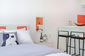 Een hotelkamer met een bed, een nachtkastje met een fles en een kaars, een spiegel en een klein tafeltje met een mandje.