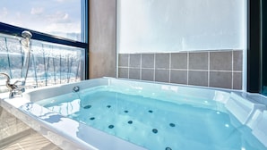 A modern bathroom with a large bathtub, a glass-enclosed shower, and a view of the cityscape. - Gapyeong Colline Pension (Gapyeong)