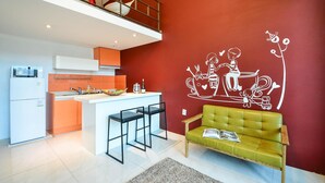 A modern kitchen with a red accent wall, a green sofa, and a white island with bar stools. - Gapyeong Colline Pension (Gapyeong)