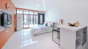 A modern hotel room with a large bed, a TV, a desk with a bowl of fruit, and a window with a view. - Gapyeong Colline Pension (Gapyeong)