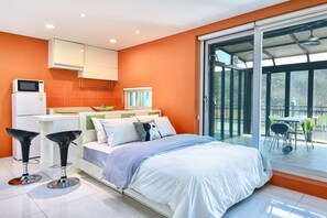 Een moderne slaapkamer met een bed, een keukenhoek en een balkon met buitenmeubilair.
