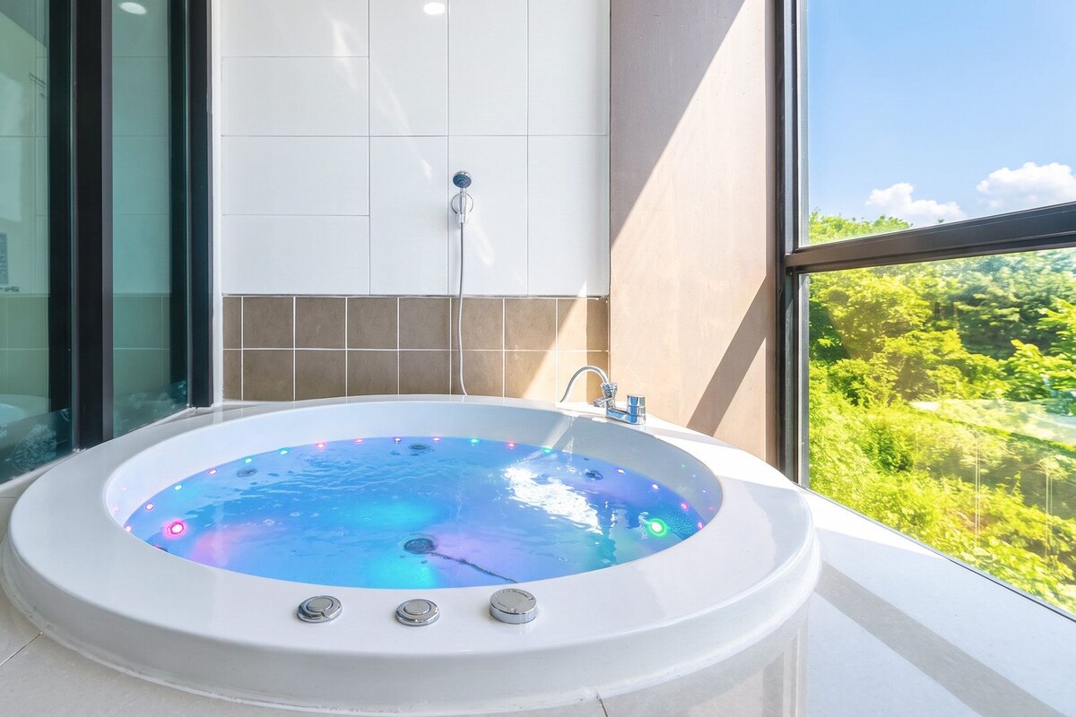 Un bain à remous avec vue sur une forêt, grâce à une grande fenêtre.