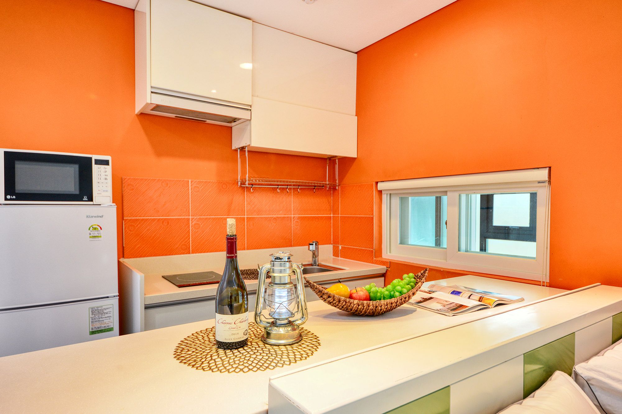 Una cocina con microondas, refrigerador, botella de vino y un frutero sobre la encimera.