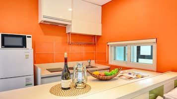 Una cocina con microondas, refrigerador, botella de vino y un frutero sobre la encimera.