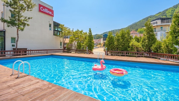 A swimming pool with two inflatable rings, a wooden deck, and a building with a 'Colline-' sign. - Gapyeong Colline Pension (Gapyeong)