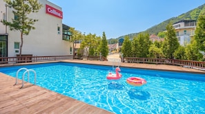 Una piscina con dos anillos inflables, una cubierta de madera y un edificio con un letrero 'Colline'.