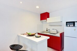 Una cocina compacta con encimera blanca, armarios rojos, un lavamanos de acero inoxidable y un microondas.
