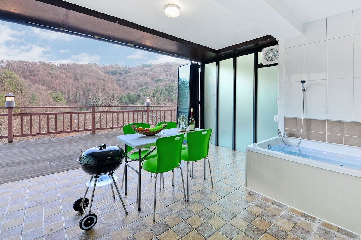Ein Balkon mit Tisch, Stühlen, einem Grill und Blick auf eine bewaldete Landschaft.