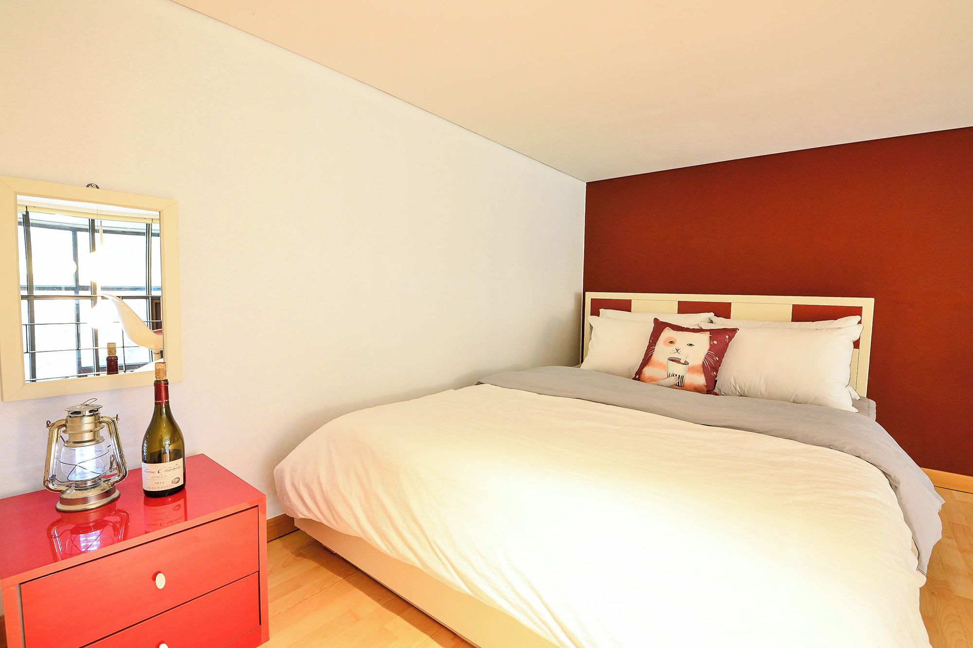A bedroom with a bed, a dresser, a bottle of wine, and a window.