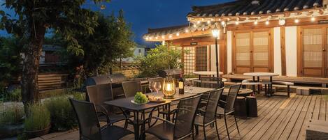 Un espace extérieur aménagé pour les repas, avec des tables et des chaises, un barbecue et une lanterne.