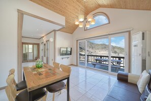 A spacious room with a wooden ceiling, a large sliding glass door leading to an outdoor deck, a wooden dining table with chairs, and a sofa. - Yeosu Healling Spa Pension (Yeosu)