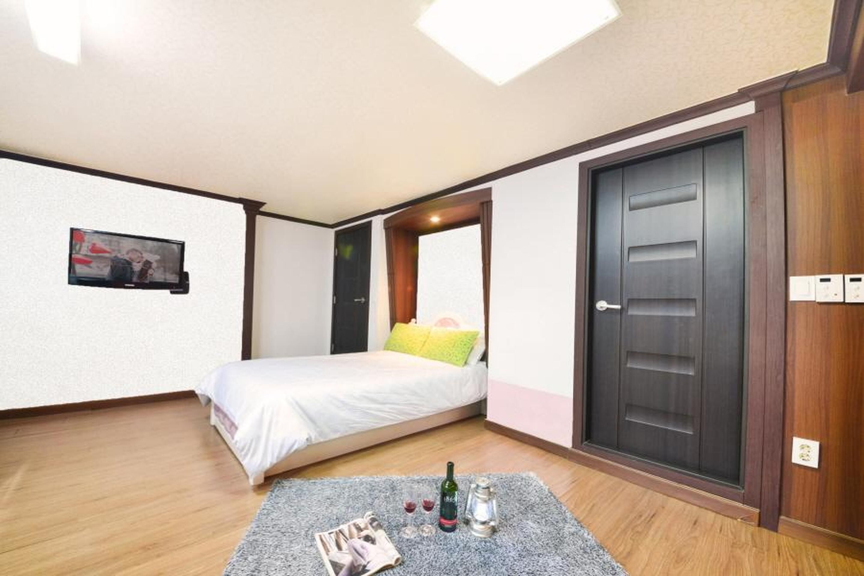 Un dormitorio con una cama, televisión, puerta y una mesita con una botella y vasos.