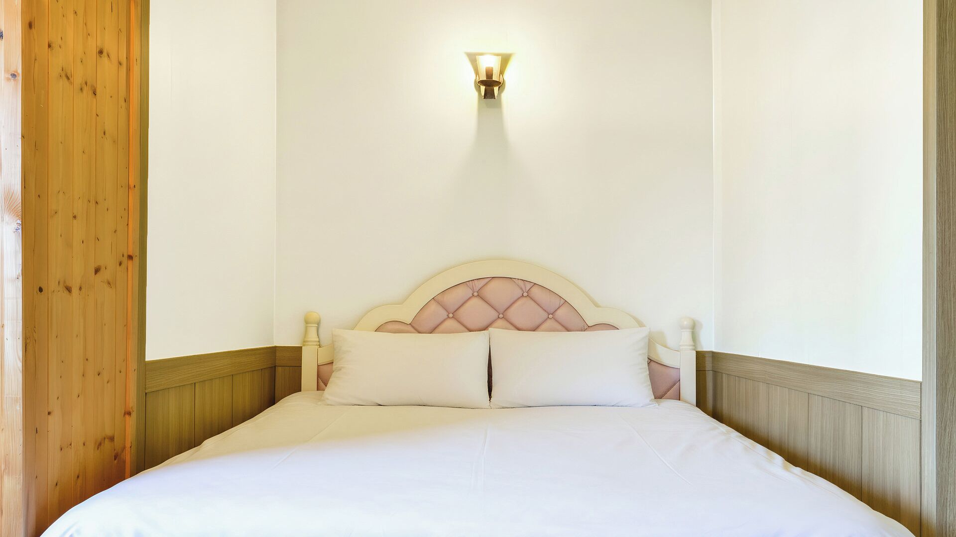 A single bed with a headboard, a wall-mounted light fixture, and wooden paneling on the walls.