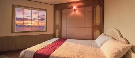 A bedroom with a bed, a window with a sunset view, and a wall-mounted light fixture.