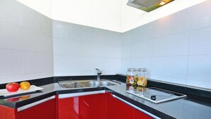 A kitchen with red cabinets, a black countertop, a sink, and a fruit bowl with apples and oranges. - Ganghwa Bettel Pension (Incheon)