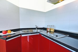A kitchen with red cabinets, a black countertop, a sink, and a fruit bowl with apples and oranges. - Ganghwa Bettel Pension (Incheon)