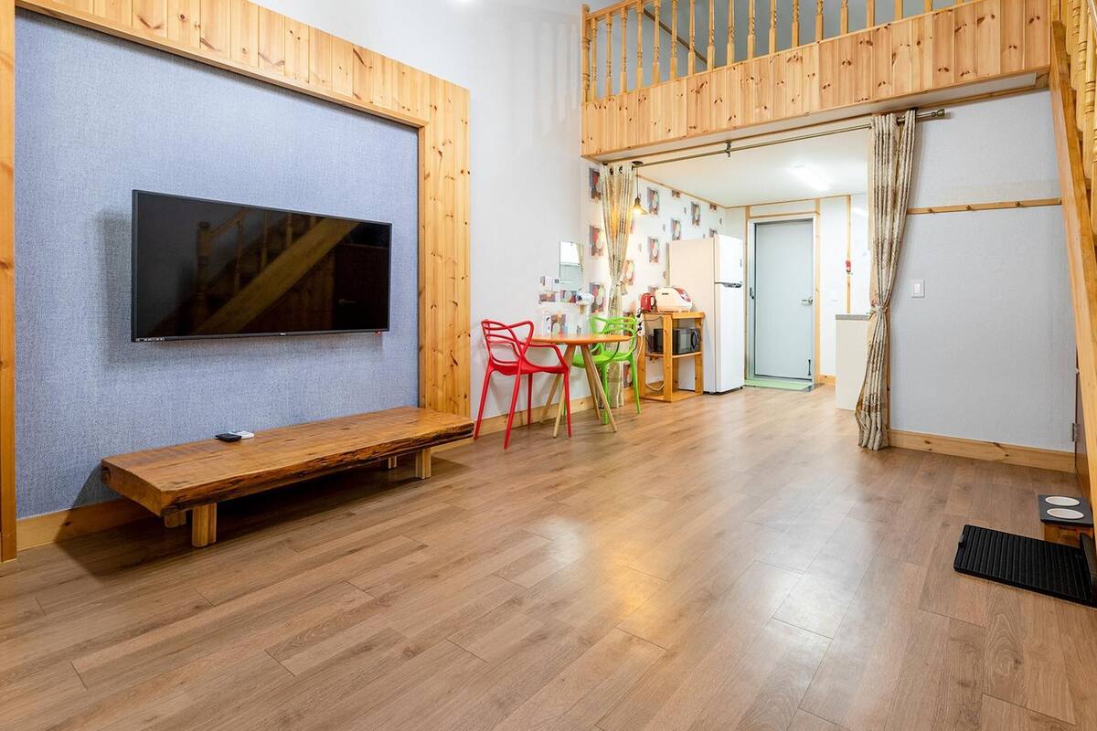 A spacious room with a wooden floor, a bench, a TV mounted on the wall, and a staircase leading to an upper level.