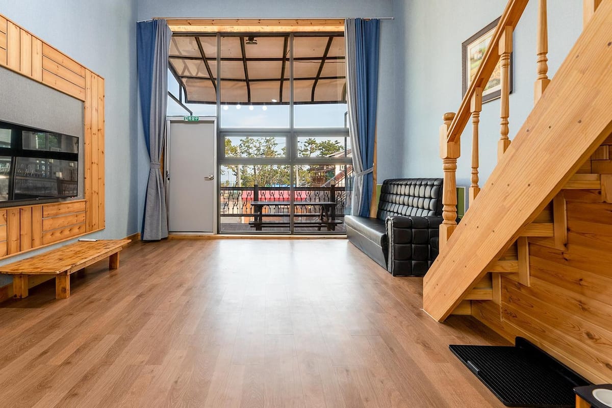 A spacious room with a wooden floor, a bench, a sofa, and a staircase.