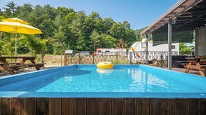 Ein Schwimmbecken mit Holzterrasse, Picknicktischen und einem gelben Sonnenschirm.