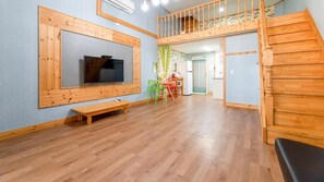 Ein geräumiges Zimmer mit einer Holzbank, einem an der Wand montierten Fernseher, einer Treppe und einem kleinen Tisch mit Stühlen.