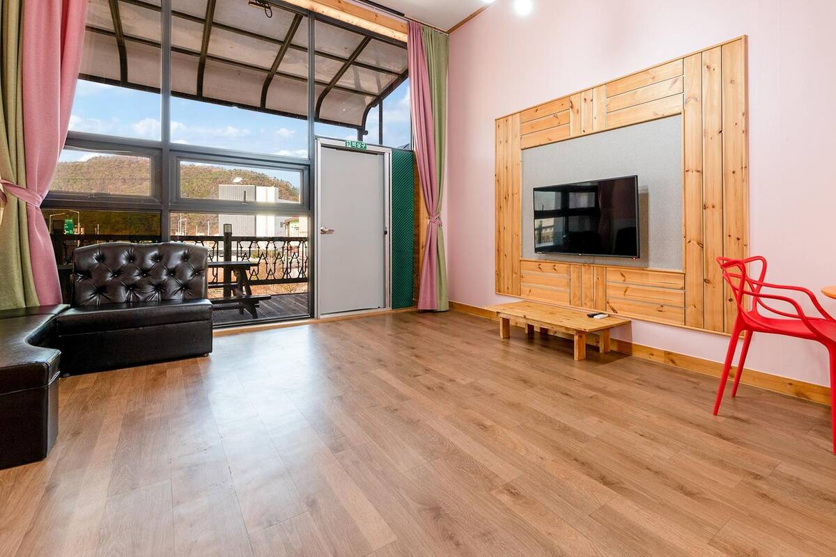 A modern living room with a large TV, a wooden cabinet, a red chair, and a sofa.