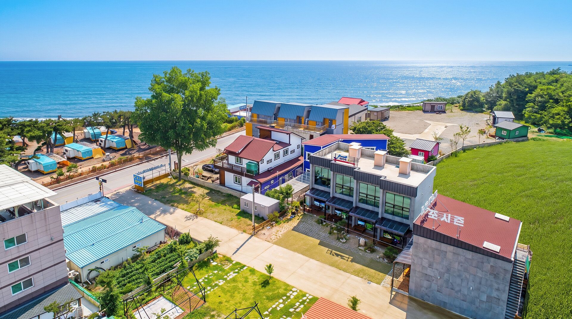 A coastal hotel with multiple buildings, including a large modern structure with a red roof and a smaller building with a blue roof.