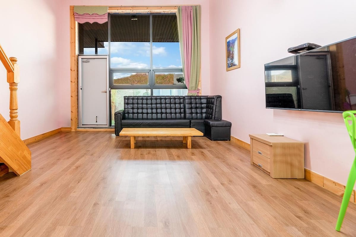 A living room with a wooden staircase, a black leather sofa, a wooden coffee table, a TV, and a small cabinet.