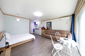 A room with a bed, a sofa, a dining table, and a chair. There is a kitchenette in the background. - Hongcheon When You Are There Pension (Hongcheon)
