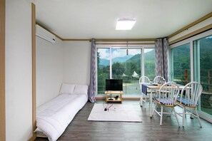 A modern room with a sofa, a dining table with chairs, a TV, and a view of mountains through large windows. - Hongcheon When You Are There Pension (Hongcheon)
