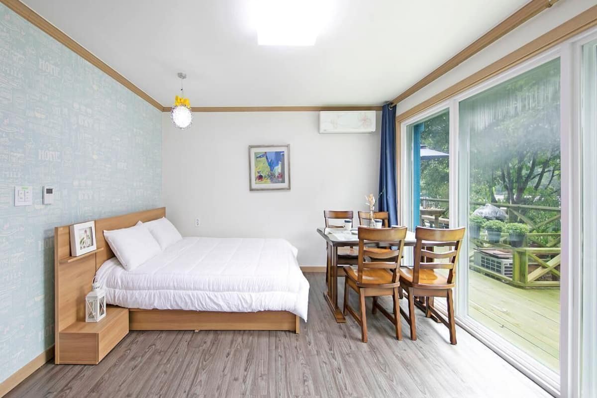 A bedroom with a bed, bedside table, lamp, and a view of the outdoors.