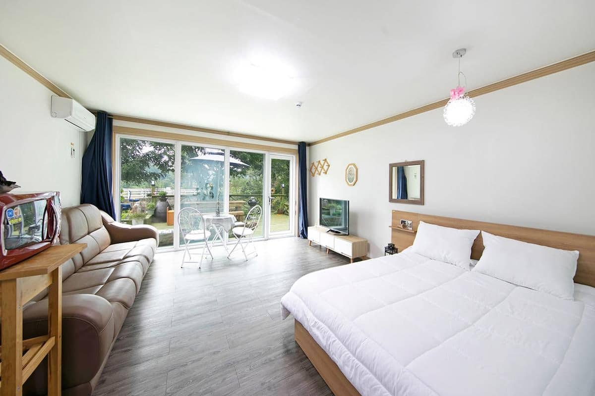 A hotel room with a large bed, a sofa, a TV, and a balcony with a table and chairs.