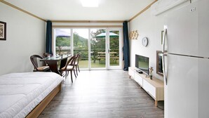 A bedroom with a bed, a TV, a dining table with chairs, and a view of a garden through a sliding door. - Hongcheon When You Are There Pension (Hongcheon)