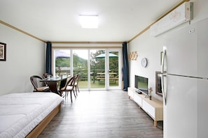 A bedroom with a bed, a TV, a dining table with chairs, and a view of a garden through a sliding door. - Hongcheon When You Are There Pension (Hongcheon)