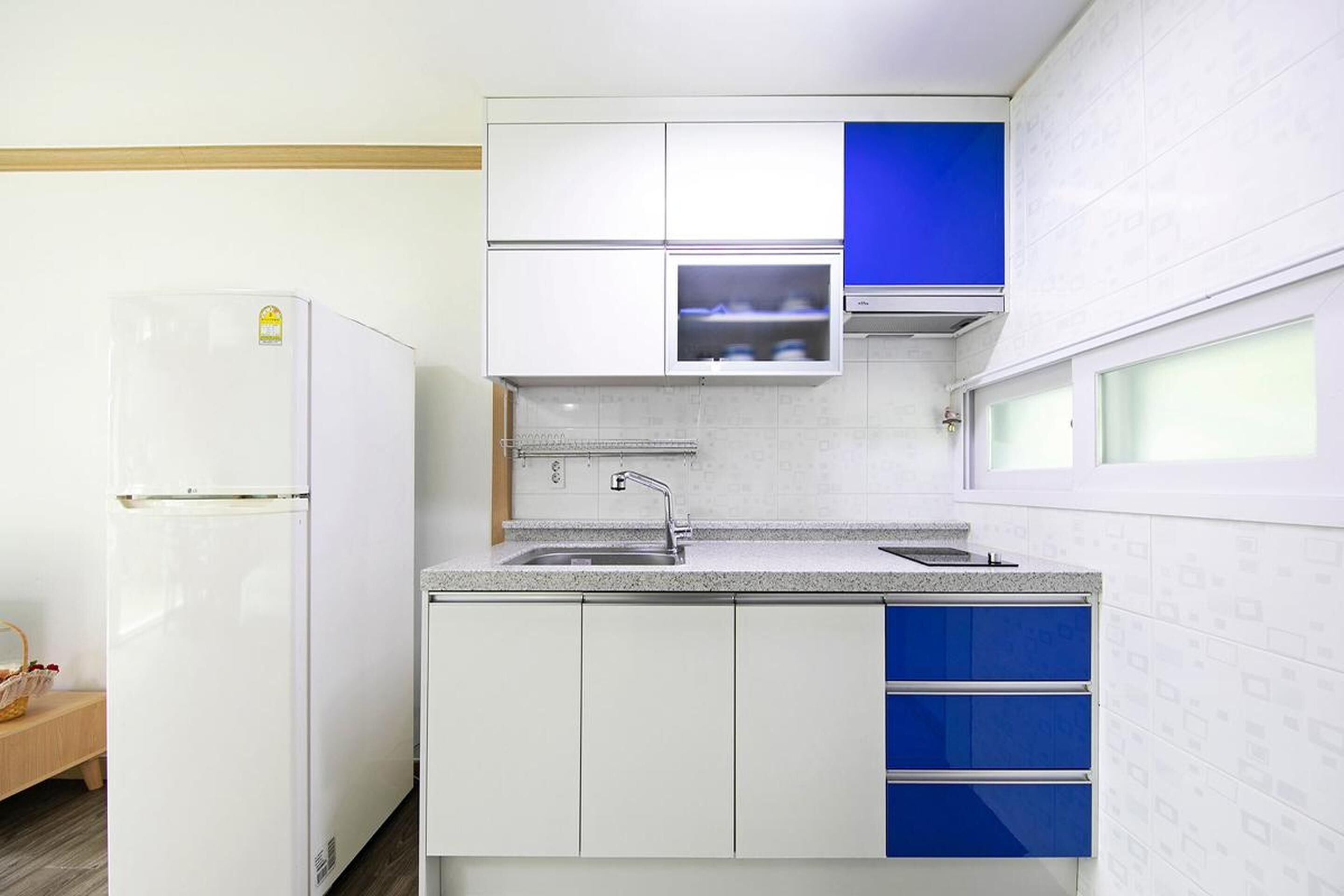 Una cocina compacta con armarios blancos, un detalle en azul, un microondas integrado y un lavamanos de acero inoxidable.