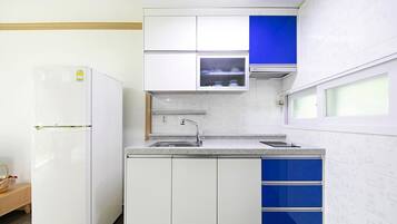 Una cocina compacta con armarios blancos, un detalle en azul, un microondas integrado y un lavamanos de acero inoxidable.