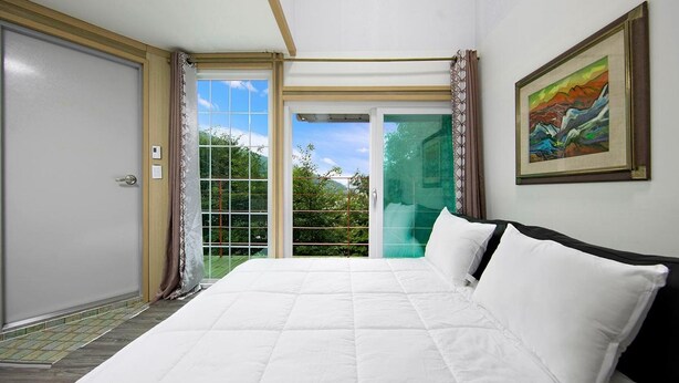 A bedroom with a large bed, a sliding glass door leading to a balcony, and a painting on the wall. - Hongcheon When You Are There Pension (Hongcheon)
