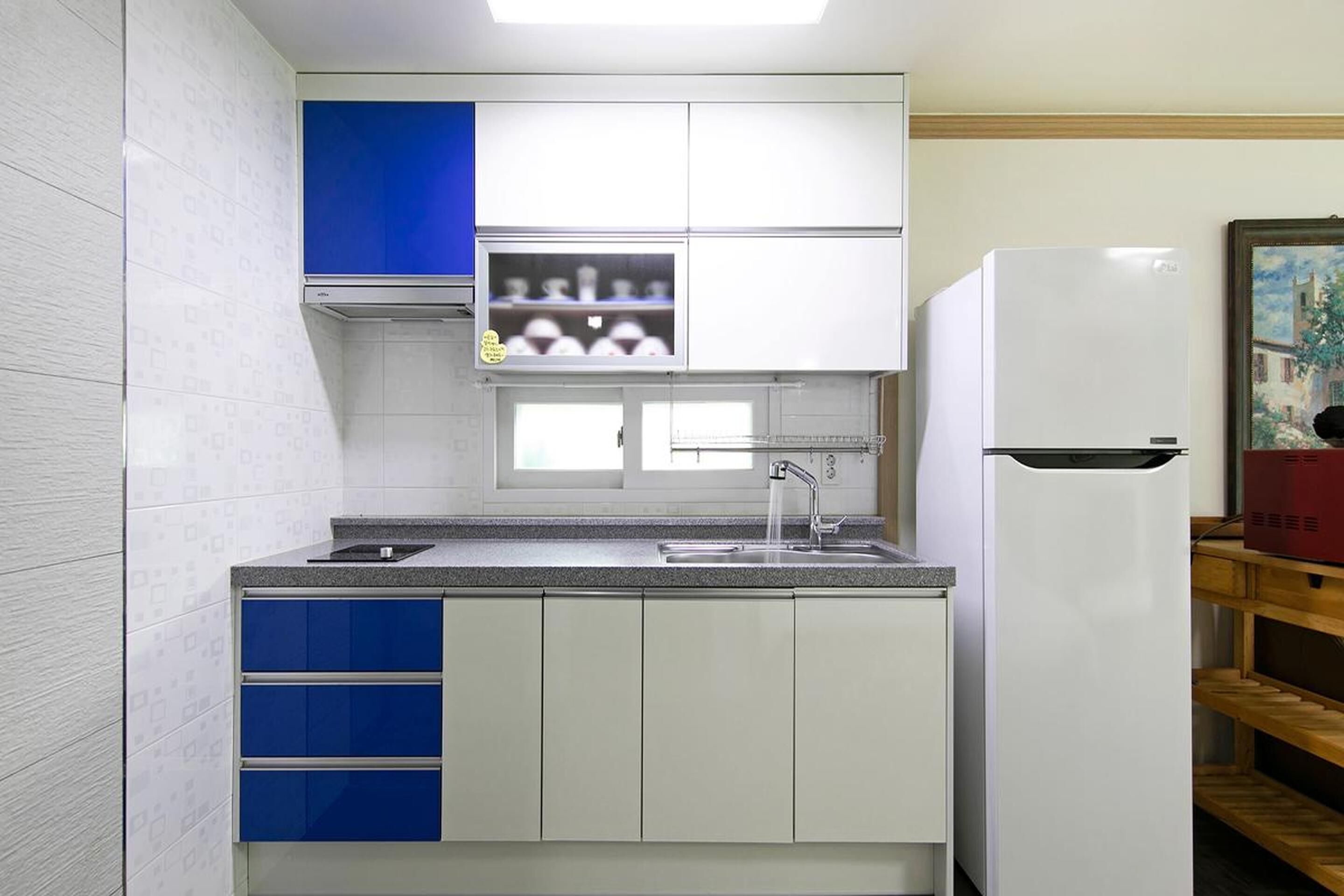 A compact kitchen with white cabinets, a blue upper cabinet, a built-in oven, and a white refrigerator.